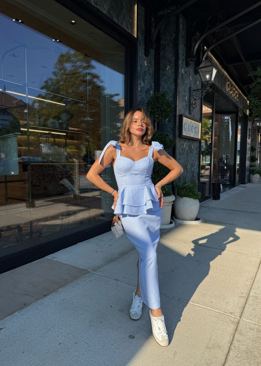 Woman in a light blue outfit standing on a sidewalk with a store in the background